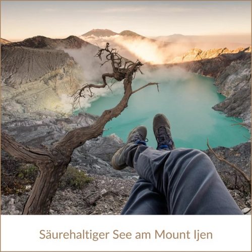 Indonesien Urlaub: Vulkanwanderung samt See am Mount Ijen, im Bild: Beine mit Wanderschuhen oberhalb eines türkisfarbenen, dampfenden, säurehaltigen Sees, neben einem verdorrten Baum