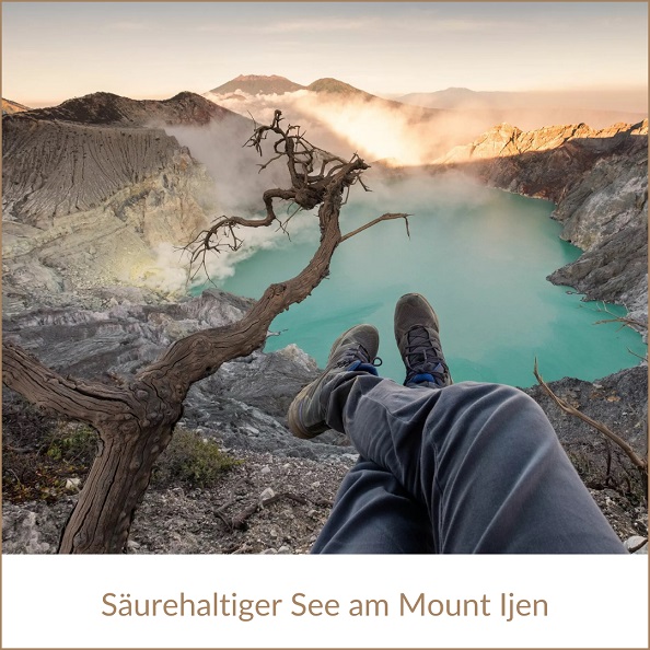 Indonesien Urlaub: Vulkanwanderung samt See am Mount Ijen, im Bild: Beine mit Wanderschuhen oberhalb eines türkisfarbenen, dampfenden, säurehaltigen Sees, neben einem verdorrten Baum