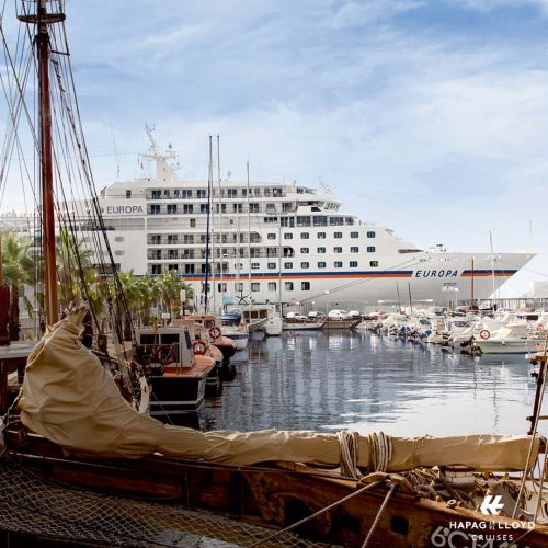 Kurzkreuzfahrt mit Stil von Hapag Lloyd Cruises, bei REISEBÜRO Wache Erfurt; im Bild: die große, weiße MS EUROPA fährt an malerischem Hafen mit schicken kleinen Segelbooten vorbei.
