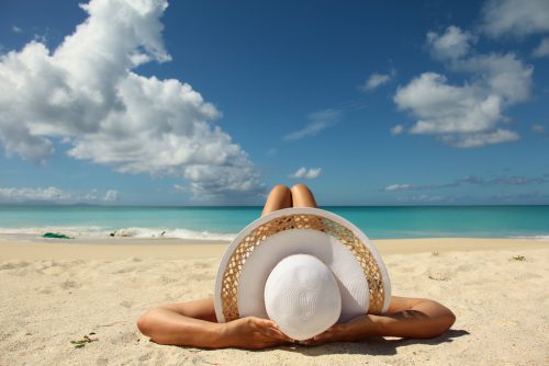 Frühbucherrabatt 2024 Reisebüro Wache Erfurt: Frau mit Sonnenhut liegt am Strand, im Hintergrund: Meer